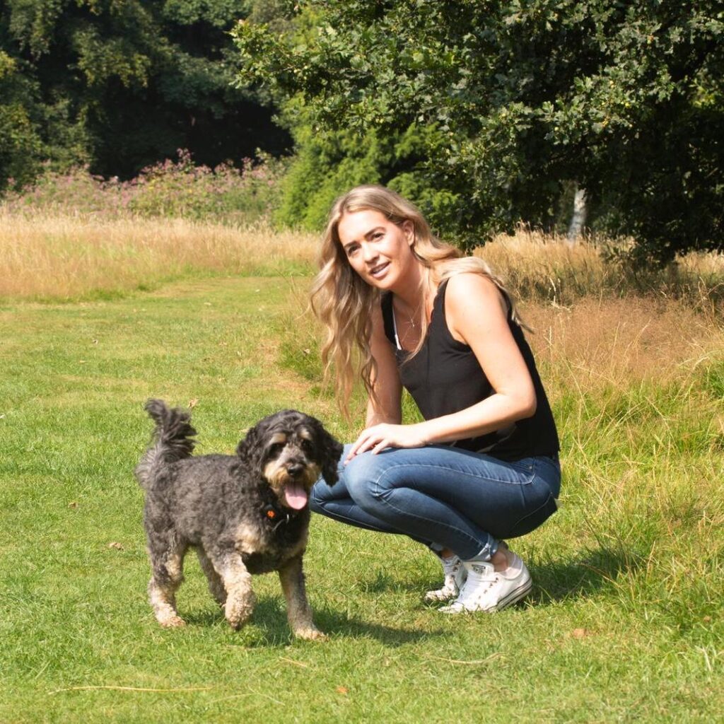 Our Founder, Becky, and her Cockapoodle Buddy, stood in a park in the sun