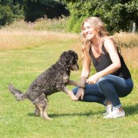 The founder of our dog owner community, Becky, and her Cockapoodle Buddy, stood in a park in the sun